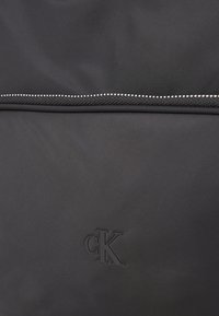 Svart tygryggsäck med en strukturerad yta, dragkedjestängning upptill och en präglad "CK"-logga på framsidan.