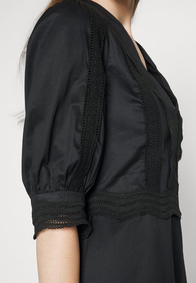 Μαύρο φόρεμα με φουσκωτά μανίκια και περίπλοκες δαντελένιες λεπτομέρειες κατά μήκος των μανικιών και του κορμού. Λείος ύφασμα με δομημένο σχέδιο.