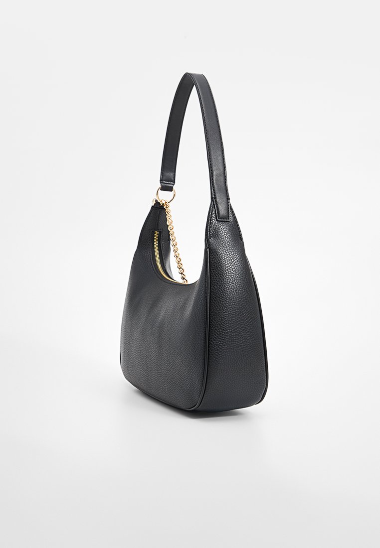 Borsa a mano in pelle nera con una texture a grana, forma curva, una sola maniglia e hardware in tonalità oro. Dettaglio di tasca con zip sul lato.