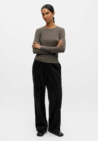 Top marrone a maniche lunghe, aderente, realizzato in tessuto leggero, abbinato a pantaloni neri in corduroy a vita alta e gamba larga con un finish testurizzato.