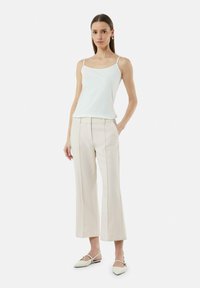 Witte mouwloze top gecombineerd met licht beige wijdlopende broeken. De outfit heeft een eenvoudig ontwerp, een gladde textuur en een getailleerde silhout. 