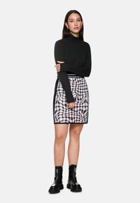 Schwarzes Langarmoberteil, kombiniert mit einem karierten Minirock in Schwarz-Weiß-Mustern. Das Model trägt schwarze Stiefeletten.