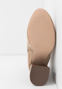 Talons en daim beige avec un bout arrondi, une texture lisse et une semelle en caoutchouc avec des rainures horizontales. Taille 37 indiquée en dessous.