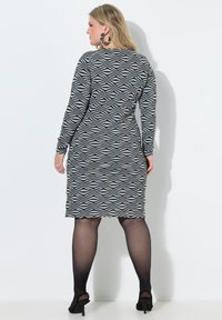 Šaty do kolen s černobílým vlnkovaným vzorem, dlouhými rukávy a přiléhavým střihem. Kombinované s průsvitnými černými punčochami a otevřenými botami na podpatku.