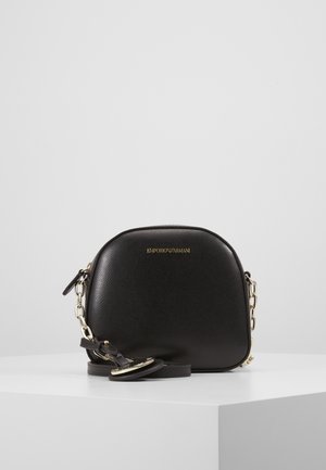 Zwarte Emporio Armani leren crossbodytas met gouden kettingriem en logo, gepresenteerd op een wit oppervlak tegen een effen grijze achtergrond.
