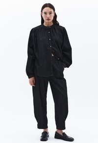Svart denim oversize-skjorta med rundad krage, knappstängning och rynkade axlar, tillsammans med matchande löst sittande byxor.