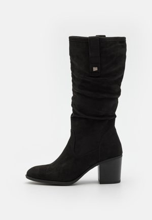 Botte hauteur genou en daim noir avec un design froissé, bout arrondi et talon bloc. Dispose d'une lanière décorative avec un accent en métal.