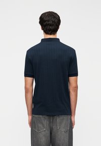 Polo bleu marine avec texture côtelée verticale et manches courtes ; présente un col à revers et un ourlet droit. Porté avec un jean gris.