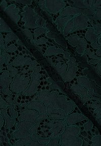 Donkergroen kantstof met ingewikkelde bloemmotieven en een textuurachtige uitstraling, met open geweven secties binnen het ontwerp.