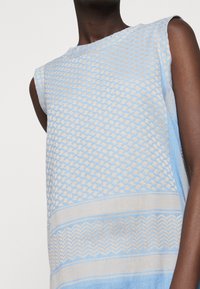 Hellblaues gestricktes Oberteil mit aufwendigen beige geometrischen Mustern, ärmelloses Design, runder Halsausschnitt und strukturierten Akzenten entlang dem Saum.