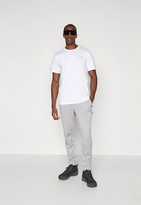 Balta T-krekls ar apaļu kaklu, pelēkas sporta bikses ar logotipu, melnas sporta kurpes un saulesbrilles. Vienkāršs dizains, viegla auduma un neitrālas krāsas.