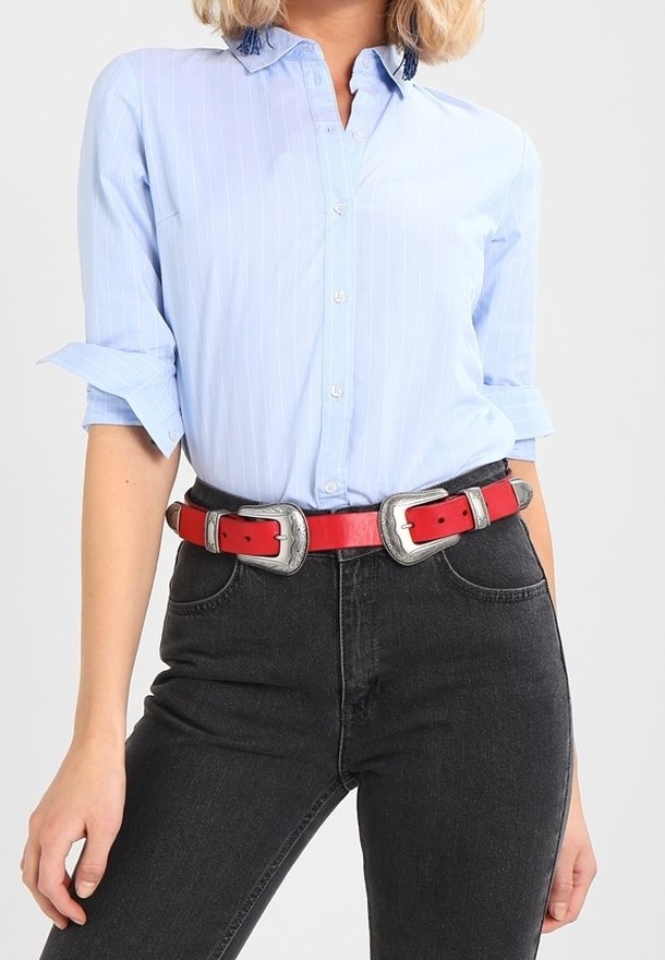Camisa de botones de color azul claro con rayas verticales blancas, mangas arremangadas, combinada con jeans negros y un cinturón rojo con detalles plateados.