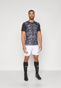 Lühikeste varrukatega must ja hall muster spordisärk, valged lühikesed püksid, mustad sokid valgete detailidega ja mustad jalatsid.