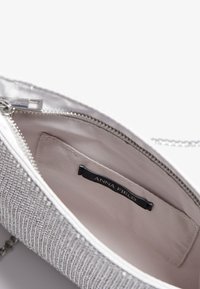 Clutch cu fermoar din material argintiu cu textură împletită. Interiorul are o căptușeală deschisă la culoare, un eticheta și un buzunar subțire pentru obiecte mici.
