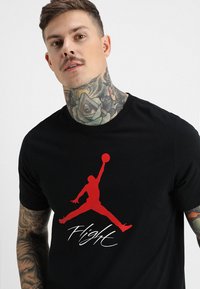 Svart bomull t-skjorte med en rød Air Jordan-logo og teksten "Flight". Rund hals og korte ermer. Glatt tekstur.