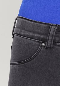 Black denim jeans with a mid-rise waistband, subtle contrast stitching, and a front pocket secured by a metallic button detail.