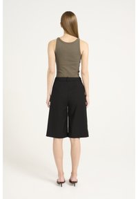 Canottiera rigata khaki abbinata a culotte nere fino al ginocchio, con cintura, tasche laterali e una texture liscia. Scarpe con tacchi alti visibili.