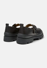 Zapatos de cuero negro con una suela de goma gruesa, que cuentan con un diseño de correa y hebilla. La costura en contraste resalta la parte superior.