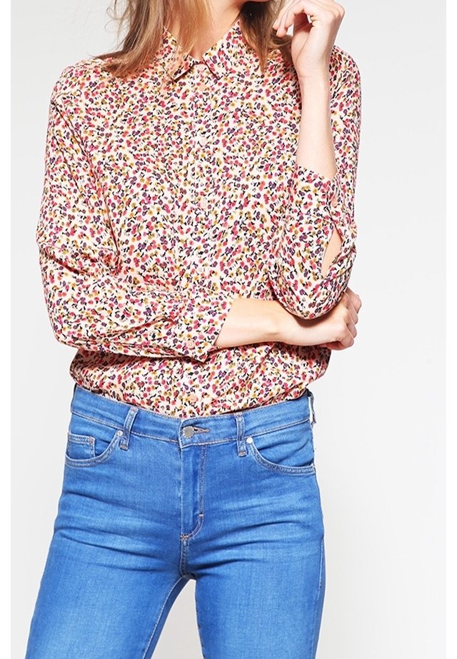 Donna che indossa una camicia a maniche lunghe con una stampa floreale multicolore infilata in jeans blu a vita alta.