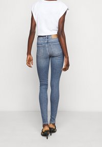 Hubené dž�íny ve světle modrém denimu, s středním pasem, zadními kapsami a nenápadnou nášivkou loga na zadní straně. Spárováno s bílým topem.