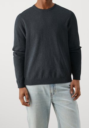 Dunkelgrauer gestrickter Pullover mit rundem Ausschnitt, gerippten Bündchen und Saum, aus einem weichen Stoff, kombiniert mit hellblauen Jeans.