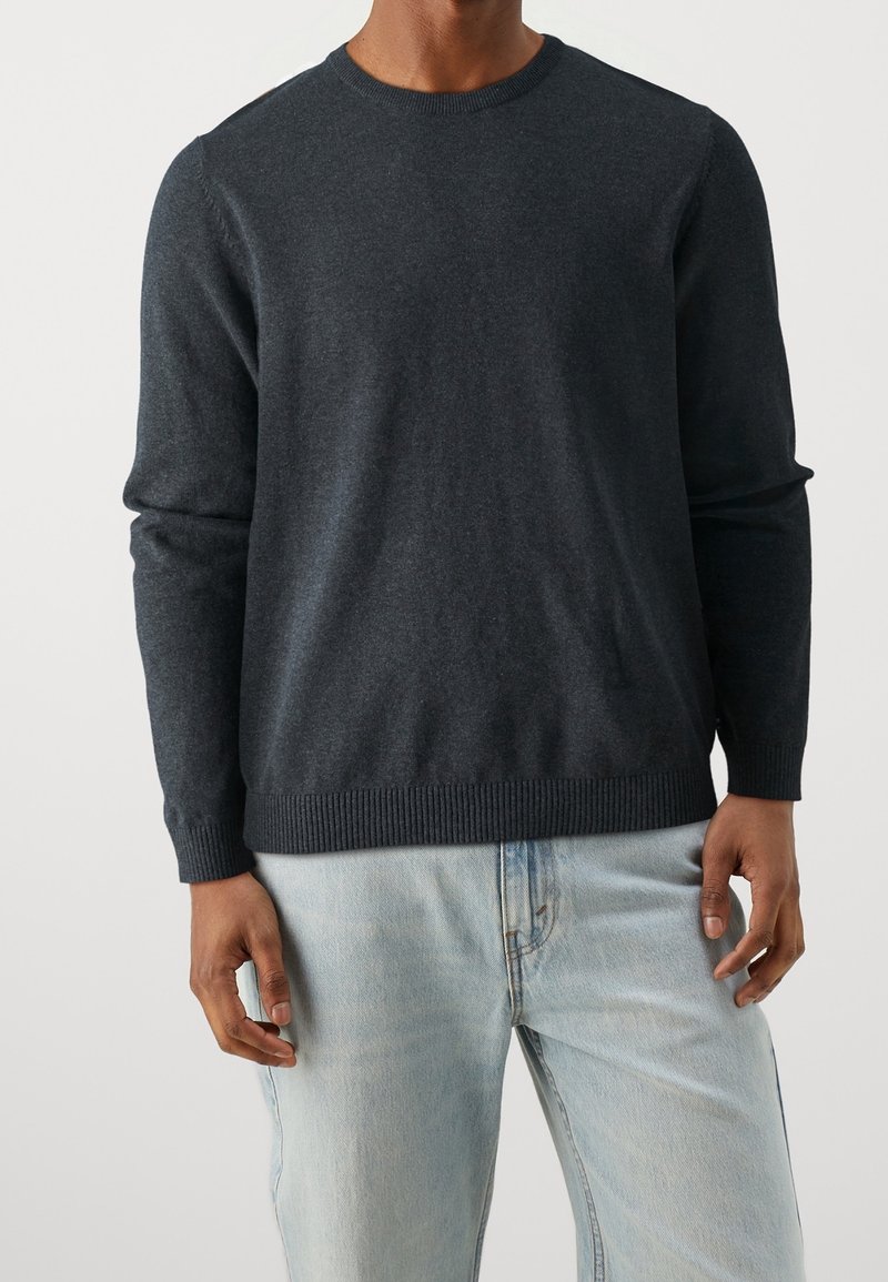 Maglione a maglia grigio scuro con scollatura rotonda, polsini e bordo a costine, realizzato in un tessuto morbido, abbinato a jeans azzurri chiari.