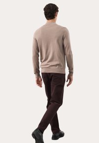 Beżowy lekki sweter z ściągaczami u rękawów i u dołu, w połączeniu z ciemno-bordowymi zwężanymi spodniami i czarnymi butami, widok z tyłu.