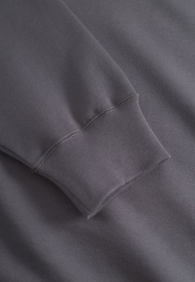 Grauer Sweatshirtstoff mit einem gerippten Bündchen und glatter Oberfläche, ausgestattet mit sichtbaren Nahtdetails und einem lässigen Schnitt.