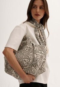 Torba na ramię wykonana z kremowego materiału z czarnym wzorem paisley. Posiada mocne uchwyty i pojemny design do noszenia przedmiotów.