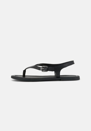 Zwarte platte sandaal met enkelriempje, teenstuk en zilveren gesp op een gladde zool, zijaanzicht op witte achtergrond.