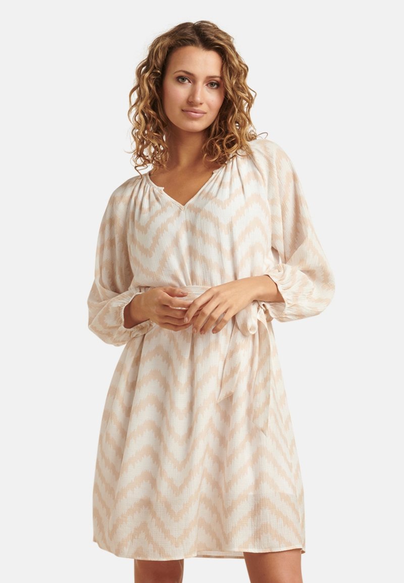 Cremefarbenes Kleid mit Chevron-Muster in hellbeige. Lange Ärmel, V-Ausschnitt, geraffte Schultern und ein Bindegürtel in der Taille. Weicher, strukturierter Stoff.