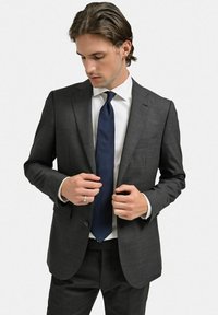 Grå kostymjacka med slim fit, i kombination med en vit skjorta och ett mörkblått slips. Anmärkningsvärda detaljer inkluderar textilstruktur och skräddarsydd design.