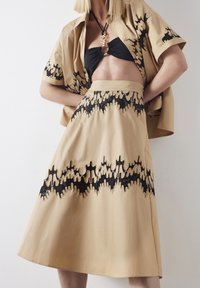 Beige twee-delige set met een cropped shirt met zwarte druppelpatroon borduursel en een bijpassende rok met een vergelijkbaar zwart ontwerp.