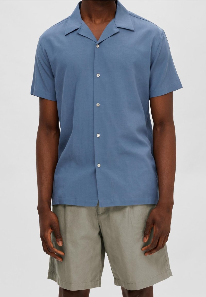 Kortärmad skjorta med krage i ljusblått tyg med mjuk textur och sex vita knappar längs framsidan. Matchad med ljusbeige shorts.