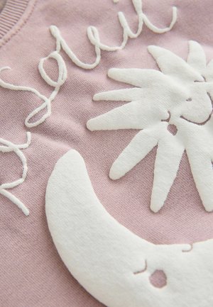 Puha rózsaszín szövet fehér, texturált nap- és holdsarló alakzatokkal, valamint díszített, írott betűs hímzett felirattal.