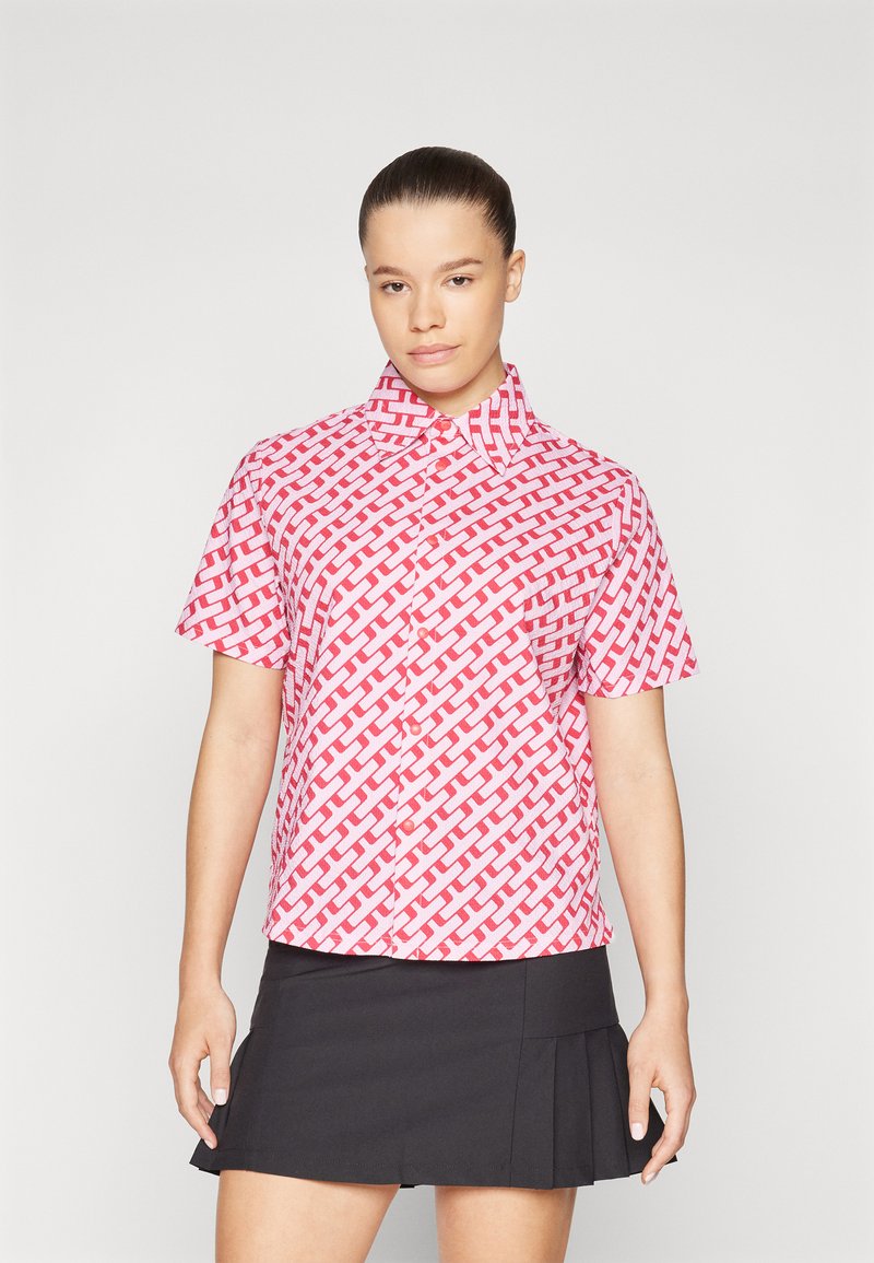 Camisa de botão de manga curta em padrão tecido rosa e branco, com gola e ajuste relaxado. O tecido tem uma textura suave.
