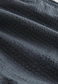 Tissu gris foncé texturé avec une apparence tissée douce, présentant un motif subtil de points en relief et de légers plis.