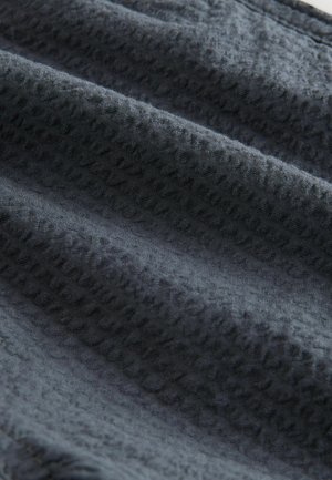 Teksturowany ciemnoszary materiał o miękkim, tkanym wyglądzie, z delikatnym wzorem wypukłych kropek i subtelnymi fałdami.