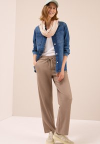 Chemise en denim bleu à boutons avec manches longues portée sur un t-shirt blanc, pantalon beige à cordon de serrage et baskets claires. Comprend une écharpe beige et une casquette claire.