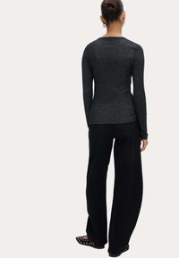 Schwarzes Langarmoberteil mit einer taillierten Silhouette aus glänzendem, strukturiertem Stoff, kombiniert mit lockeren, schwarzen weit geschnittenen Hosen und flachen schwarzen Schuhen.