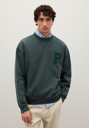 Dark green sweatshirt in a soft material, featuring a textured letter "P" on the chest, paired with a light blue striped shirt underneath.
