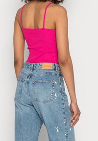 Hetrosa rosa ribbad linne med tunna axelband, i kombination med ljusblå slitna jeans, dekorerade med färgfläckar och en logo patch i tan läder.