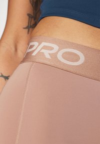 Jasnoróżowe legginsy sportowe o miękkiej fakturze, z szerokim beżowym elastycznym pasem z białym nadrukiem "PRO".