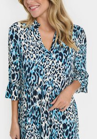 Mėlyna ir juoda leopardų rašto suknelė su V formos iškirpte, ilgomis rankovėmis ir plačiomis alkūnėmis. Lengvas audinys, sluoksniuota konstrukcija ir laisvas kirpimas.