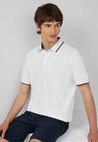 Witte polo shirt met marineblauwe kraag en manchetten, met drie knopen en een klein geborduurd logo. Gedirigeerd met marineblauwe shorts.