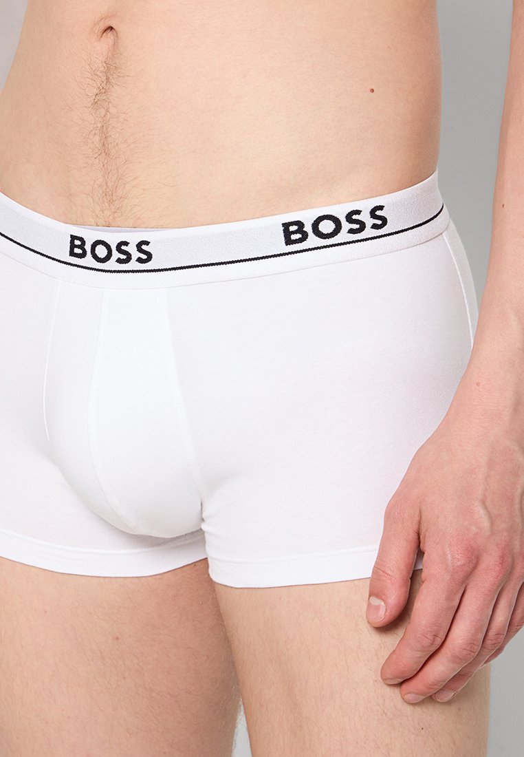 Boxers de algodón blanco con una cinturilla elástica negra que presenta la palabra "BOSS" repetida. Textura suave, diseño ajustado y longitud hasta media thigh.