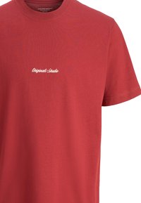 Red cotton T-shirt with a crew neck and short sleeves; features white embroidered text "Originals Studio" on the chest.