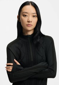 Czarna bluza zapinana na zamek, z teksturowanymi wzorami, wysokim kołnierzem i długimi rękawami z otworami na kciuki. Materiał wydaje się gładki i dopasowany.