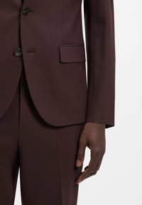 Bordeauxroter Anzugsakko mit strukturiertem Design, texturiertem Stoff, einer Brusttasche und schwarzen Knöpfen auf der Vorderseite. Gezeigte maßgeschneiderte Passform.