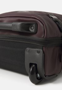 Rolling suitcase with a maroon waterproof exterior and black fabric base. Features a retractable handle, zipper closure, and sturdy wheels.
